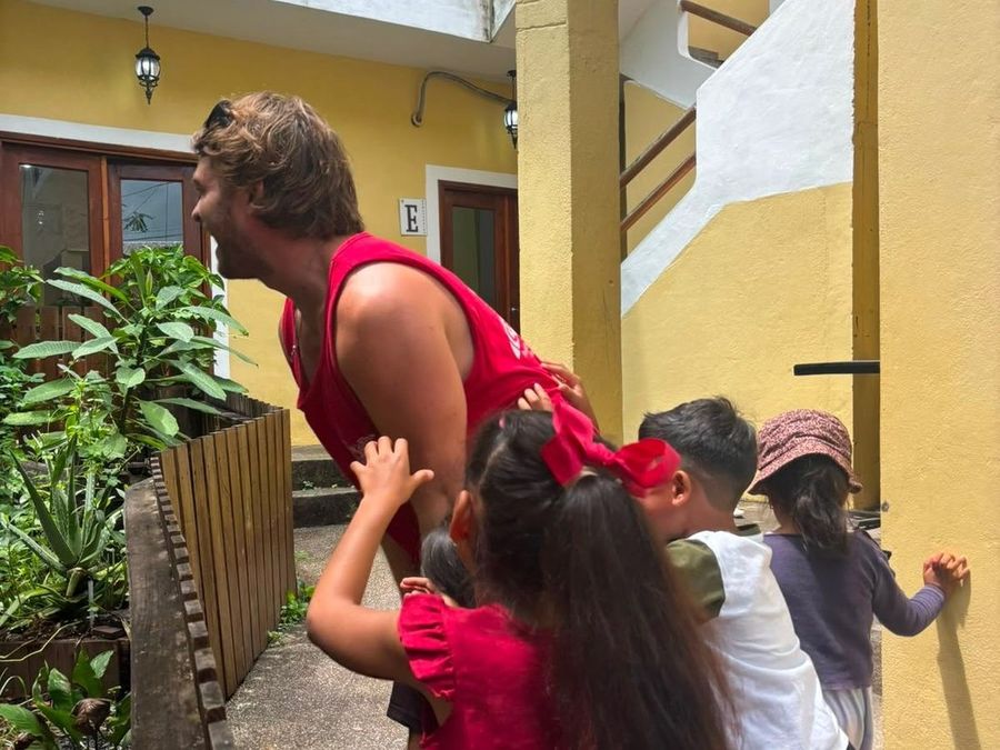 Ian, de perfil, con cuatro niños que se acercan y se reúnen a su alrededor en un patio.