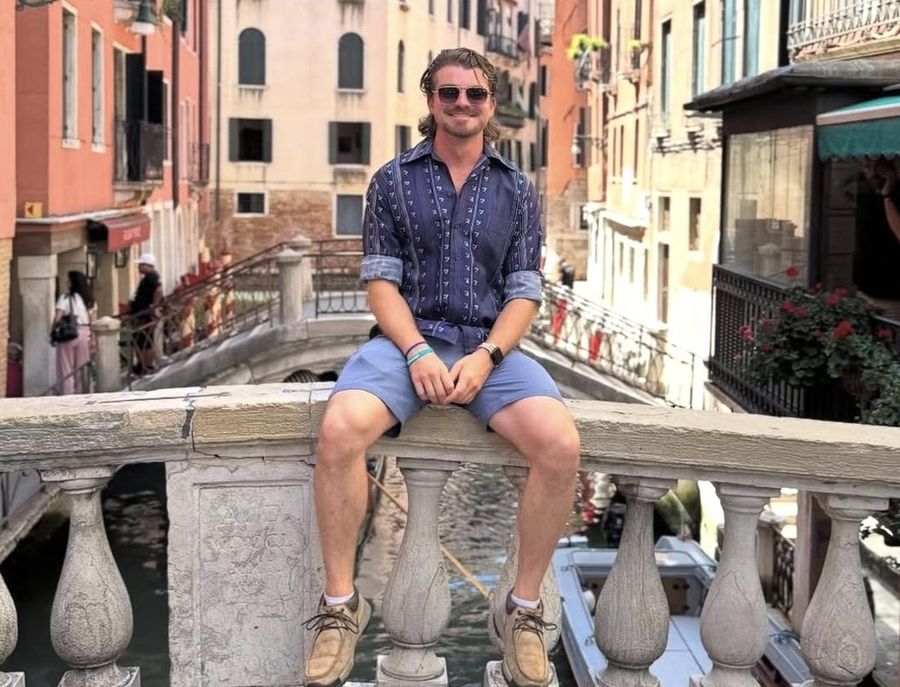 Ian Treger sentado en el pretil de un puente de piedra sobre un canal en Venecia.