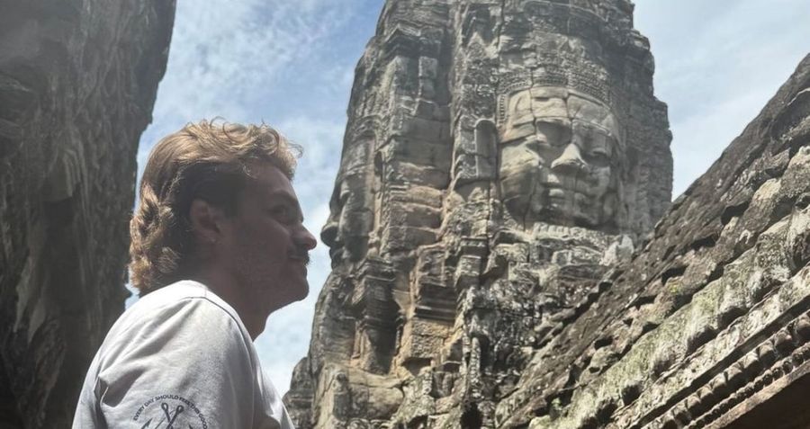 Ian Treger mirando hacia un rostro de piedra tallado en una torre de Angkor Thom, Camboya.