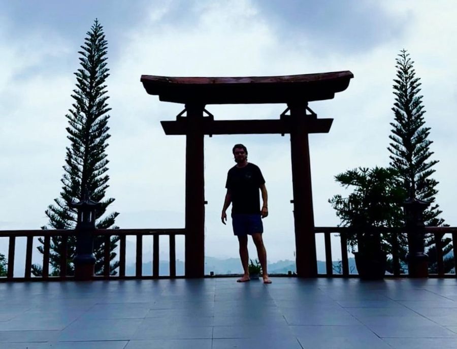 Ian en silueta bajo un torii al atardecer, en Asia.