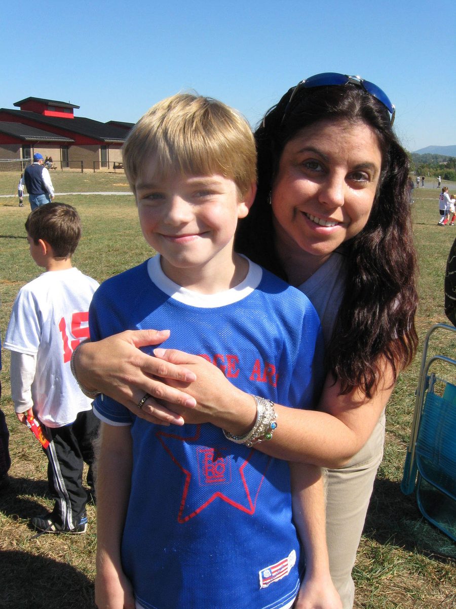 Ian de niño, con una camiseta azul de fútbol, abrazado por su tía Celine al costado de una cancha.