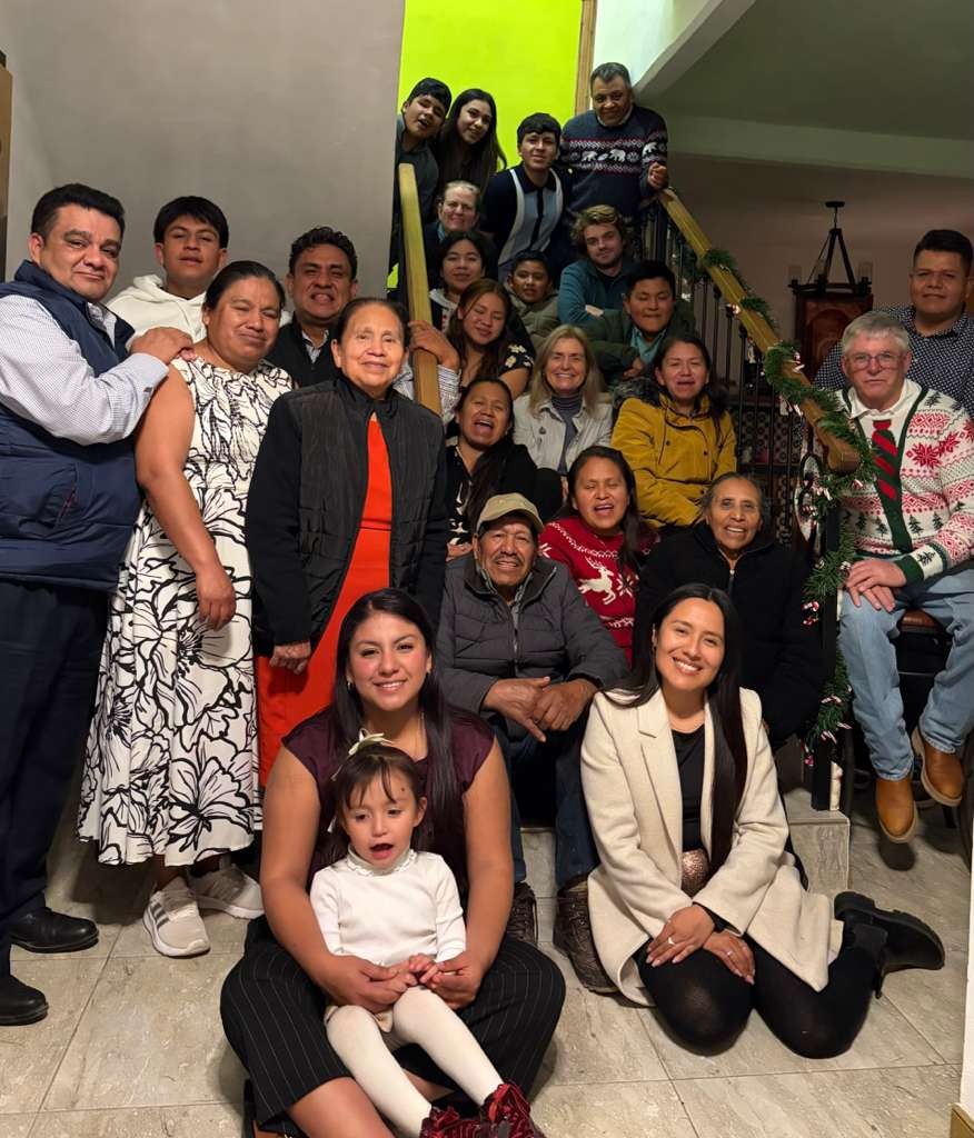 La familia extendida y los amigos cercanos de Ian en México, más de veinte personas de todas las edades posando juntas en una escalera decorada con guirnaldas navideñas.