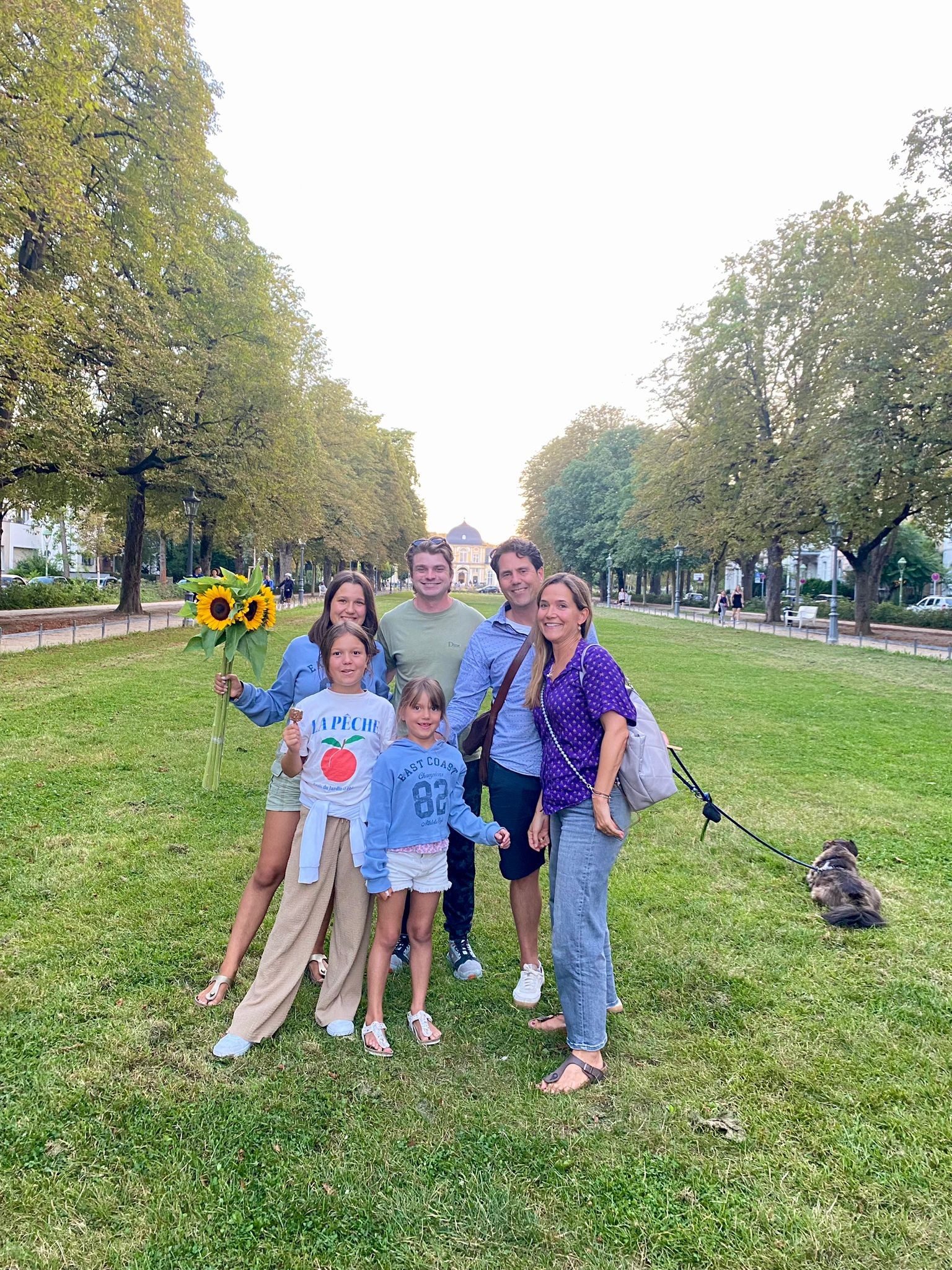 Ian, con los lentes de sol sobre el pelo, de pie junto a su familia anfitriona alemana &mdash; dos padres, tres hijos y su pequeño perro con correa &mdash; en un bulevar arbolado y con césped, uno de ellos sosteniendo un ramo de girasoles.