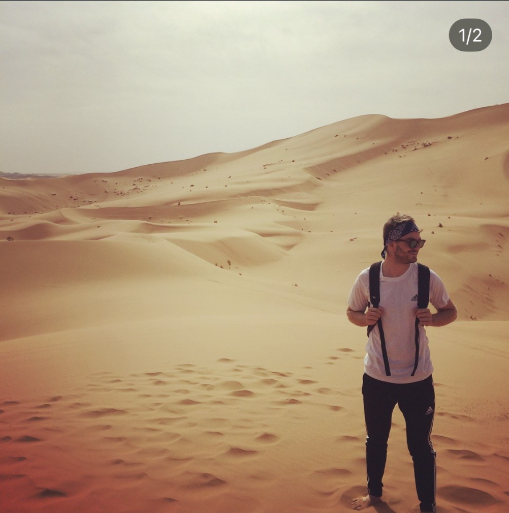 Ian, con una bandana estampada y una mochila, de pie entre las dunas de arena del desierto del Sahara, en Marruecos.